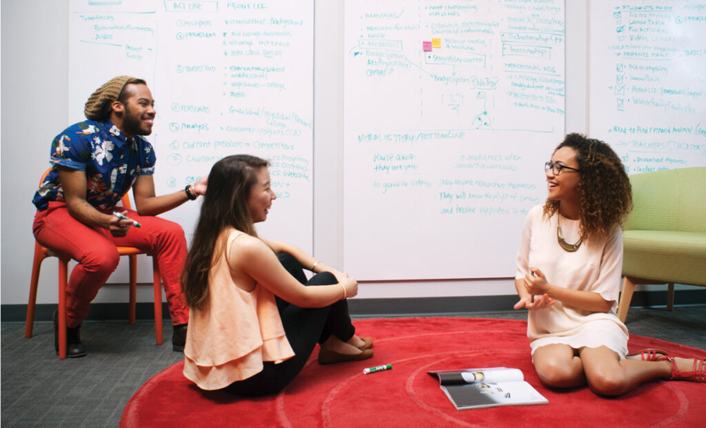 Three students collaborating by a large whiteboard wall